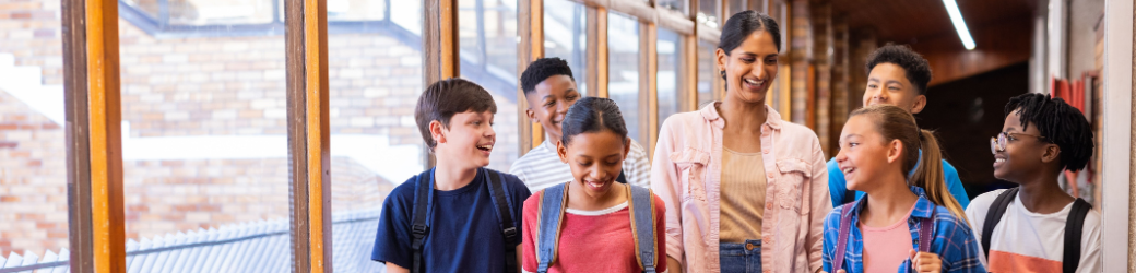 A teacher and a diverse group of smiling students walking down a school hallway.