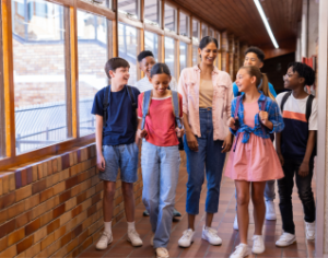 A teacher and a diverse group of smiling students walking down a school hallway.